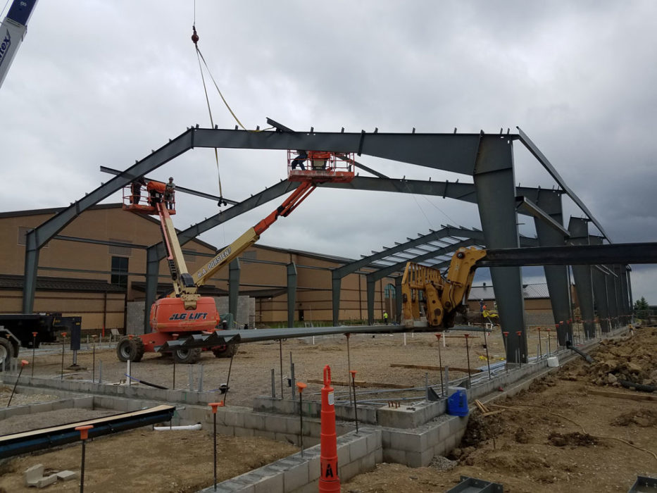 Workers in lifts and cranes setting structural steel for school building.