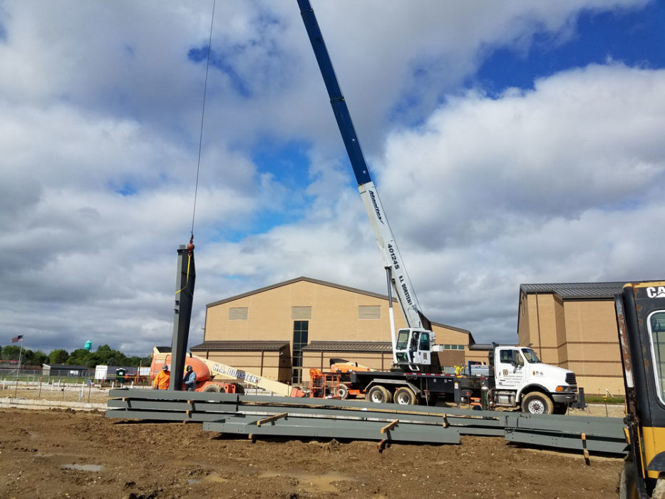 Crane lifting steel beams for school building under construction.