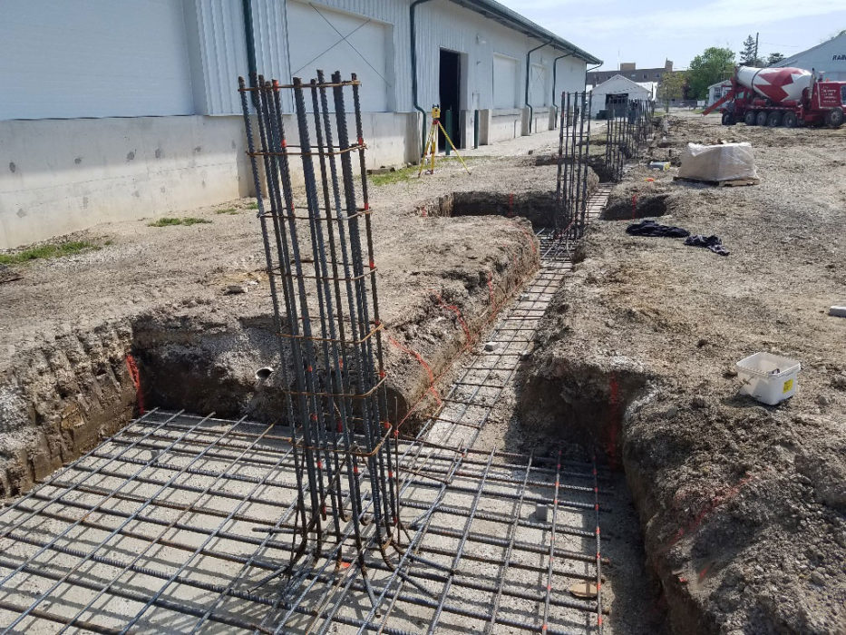 Excavated foundation with reinforcing steel placed and concrete being poured.