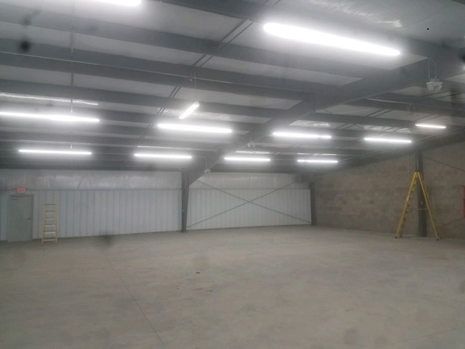 Interior of custom-engineered metal building under construction with concrete floor slab and lighting.